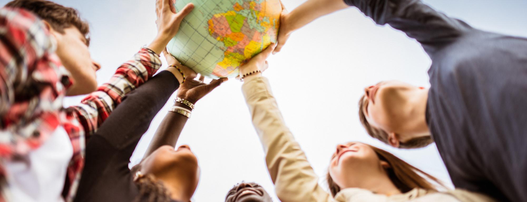 A group of young people with their hands on a globe, raising it to the sky.
